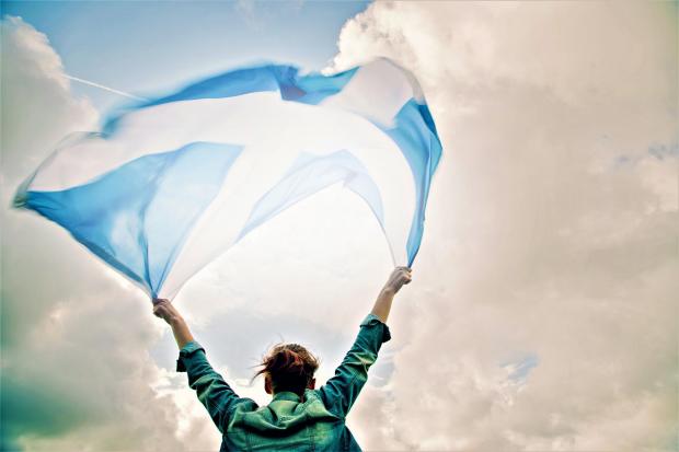 Young woman holding up a Scottish flag letting it fly in the wind above her head.