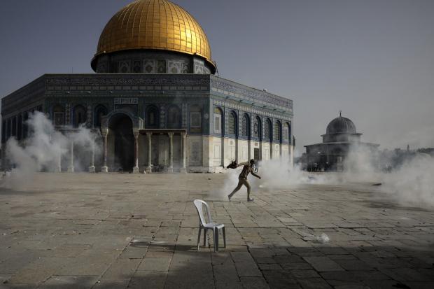 A Palestinian man run away from tear gas during clashes with Israeli security forces in front of the Dome of the Rock Mosque at the Al Aqsa Mosque compound in Jerusalem's Old City Monday, May 10