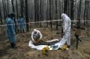 Experts search the body of a Ukrainian soldier during an exhumation in the recently retaken area of Izium, Ukraine, Friday, Sept. 16, 2022.