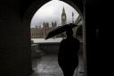 A member of the public holds an umbrella while looking across the Thames to the Palace of Westminster