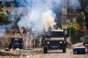 TOPSHOT - Israeli soldiers fire tear gas canisters from an armoured vehicle during an ongoing military operation in the occupied West Bank city of Jenin on July 4, 2023.