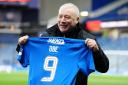 Former Rangers player Ally McCoist holding a shirt with the letters OBE