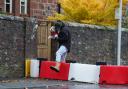 A man lifts his dog over a flood defence barrier erected on Church Street in Edzell, Angus