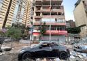 Damaged cars are parked in front of a building that was hit by an Israeli airstrike