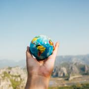 A person holding a planet Earth against a mountainous landscape. Credit: Canva