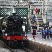 Piper Kevin MacDonald from the Red Hot Chilli Pipers with schoolchildren from the Royal Scottish Country Dance Society, during an event at Edinburgh Waverley station to mark the day the world famous locomotive, Flying Scotsman, entered service on