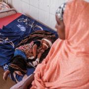 A malnourished child rests on a bed as a woman sits next to him at the nutrition unit of the Gode General Hospital, in the city of Gode, Ethiopia, on January 13, 2023