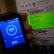 A handheld SSE smart meter for household energy usage is held next to an electricity meter