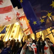 TOPSHOT - Protesters wave Georgian national and European flags during a demonstration outside the parliament building as they protest against a draft bill on 