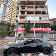 Damaged cars are parked in front of a building that was hit by an Israeli airstrike