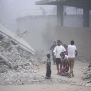 Palestinians walk through dust by the rubble of houses, destroyed by Israeli strikes in Khan Younis, Gaza Strip