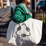 A young woman carrying a reusable shopping with a recycling symbol.