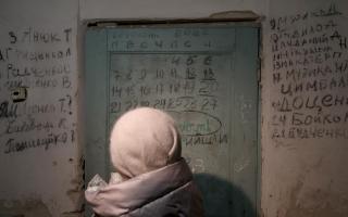 YAHIDNE, UKRAINE - JANUARY 17, 2024 - A woman faces the door with the calendar and names of the people who died in the basement of the school where Russian occupiers held more than 300 residents, including 77 children