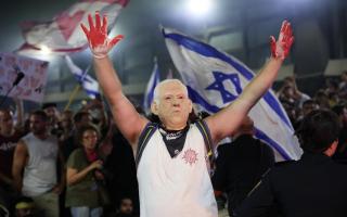 TOPSHOT - A protester, wearing a mask depicting Israel's Prime Minister Benjamin Netanyahu, raises his hands wearing gloves with red paint, during an anti-government rally calling for the release of Israelis held hostage by Palestinian militants in