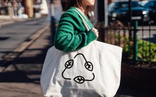 A young woman carrying a reusable shopping with a recycling symbol.