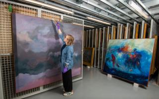 Exhibition curator, Kirsty Matheson, dusting Jon Schueler's Storm at Sea Remembered ahead of it being installed